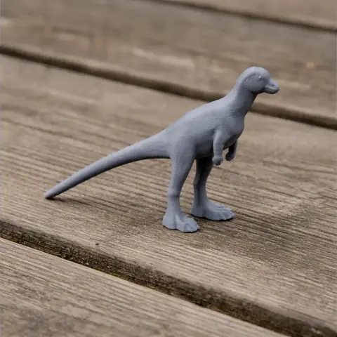 A gray 3D-printed dinosaur model with a long tail and short arms on a wooden surface.