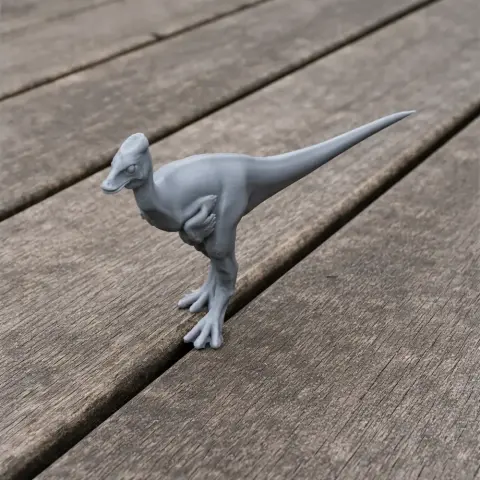 A small, gray 3D-printed dinosaur model stands on a wooden surface.