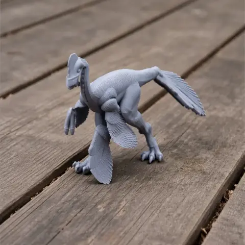 Gray 3D-printed model of a feathered prehistoric creature with a beak, on a wooden surface.