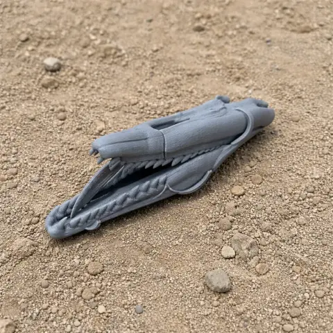 Gray 3D-printed dinosaur-like skull model resting on rough, sandy terrain.