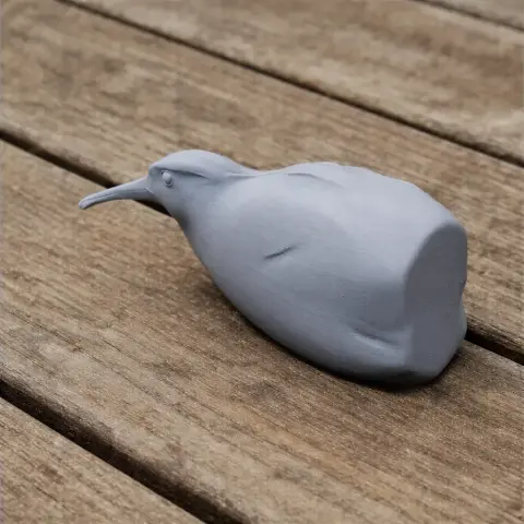Gray 3D printed model of a bird with a long beak, resting on a wooden surface.