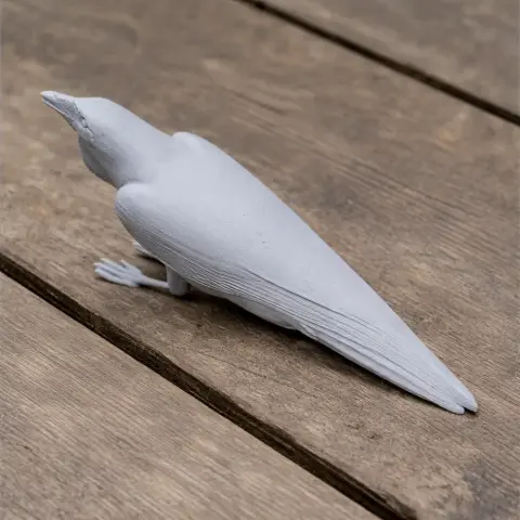 3D printed model of an Australian raven bird in a resting position on a wooden surface.