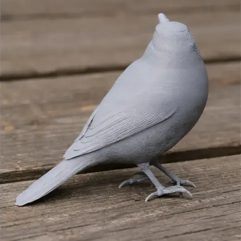Gray 3D-printed model of a bird, standing on a wooden surface, with detailed feathers and claws.