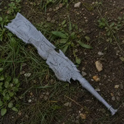 A detailed, ornate fantasy sword prop with intricate designs lies on grass and dirt.