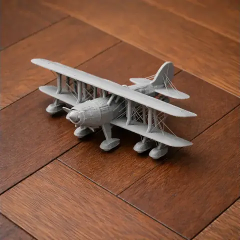 Gray 3D-printed model of a biplane with intricate wing details on a wooden surface.