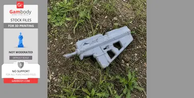 A gray 3D-printed futuristic gun prop lying on grass and soil.