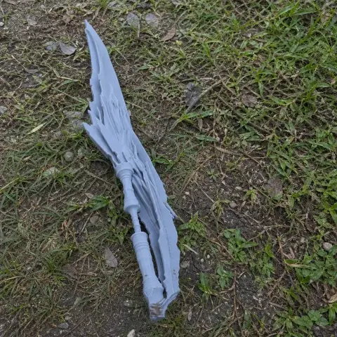 Intricately detailed, jagged sword prop with distinctive edges, lying on a grassy ground.