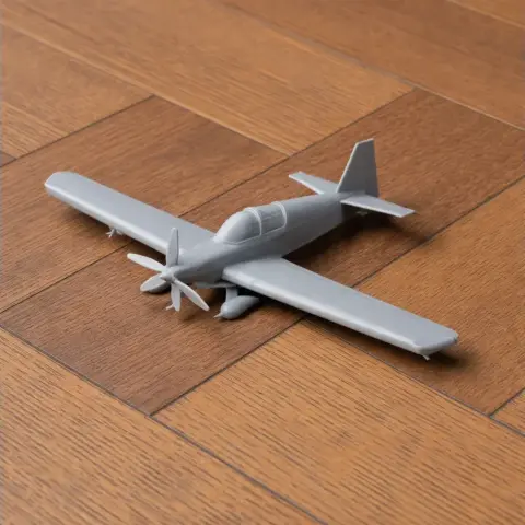 Gray scale model of a propeller aircraft on a wooden floor.