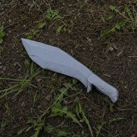 A white, 3D-printed kukri prop lies on grass and dirt.