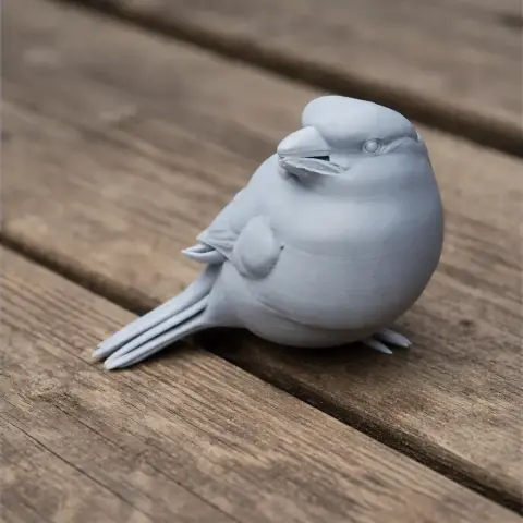 A 3D printed model of a round bird with a smooth surface, sitting on a wooden surface.