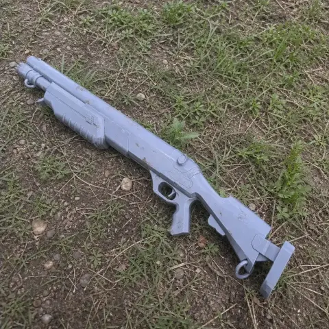A gray, 3D-printed futuristic rifle prop, placed on grass outdoors.