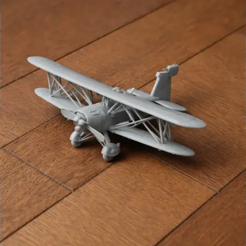Grey 3D-printed biplane model sits on a wooden surface, showcasing detailed wings and struts.