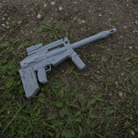 A gray, 3D-printed sci-fi rifle prop on grass and soil.