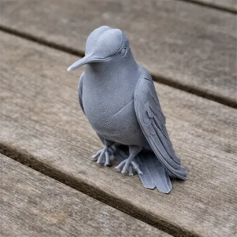 Gray 3D-printed model of a hummingbird, sitting on a wooden surface.