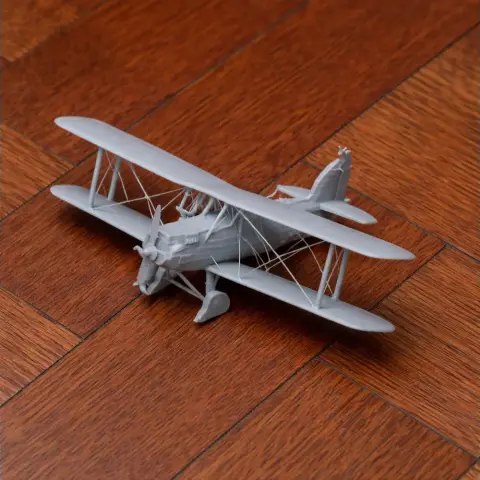 A detailed 3D-printed model of a biplane on a wooden floor.
