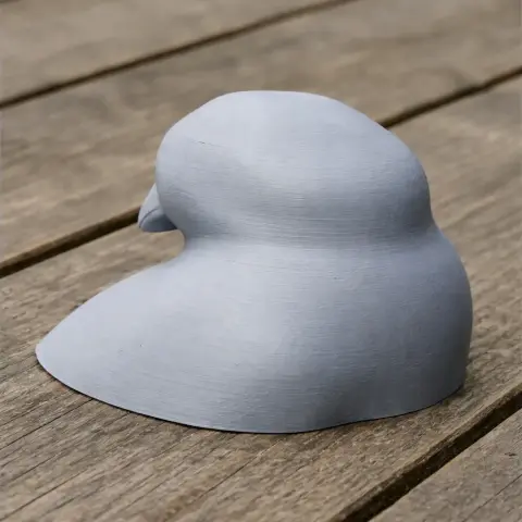 3D print model of a stylized bird head, positioned on a wooden surface.