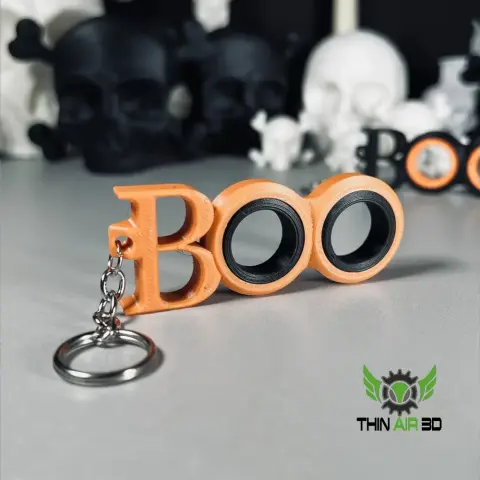 Orange 'Boo' fidget spinner keychain with silver ring, set against a backdrop of skulls.