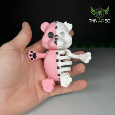 A half-pink, half-skeleton cartoonish bear figure held in a person's hand.