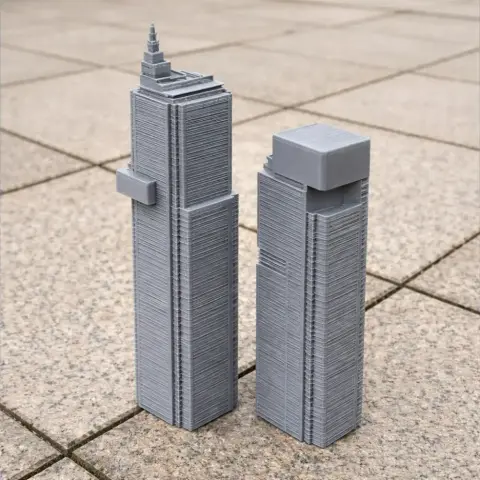 Two gray 3D-printed models of modern skyscrapers with distinct roof designs on a patterned surface.