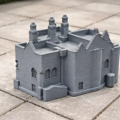 Gray 3D printed model of Aydon Castle, featuring chimneys and arched windows, set on a tiled surface.