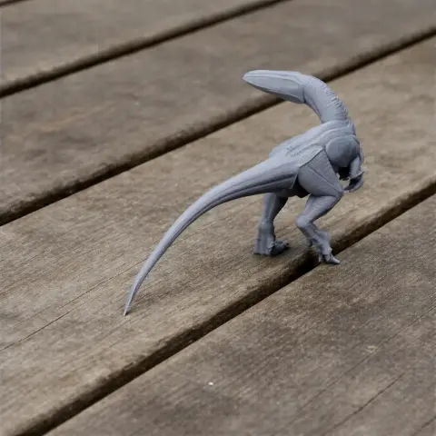 Gray 3D-printed dinosaur model with long tail and raised head, standing on wooden slats.