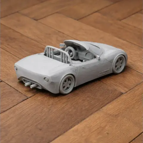 Gray 3D-printed model of a convertible sports car on a wooden surface.