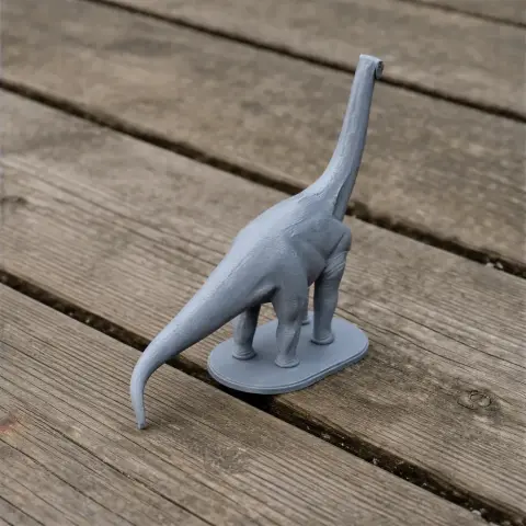 Gray 3D-printed model of a long-necked dinosaur on a wooden surface.