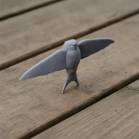 Gray 3D-printed model of a Bahama swallow with wings spread, standing on a wooden surface.