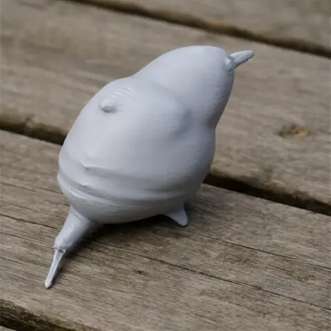 Gray 3D-printed model of a plump bird with a pointed beak and tail, on a wooden surface.