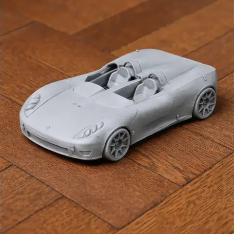 A gray 3D printed sports car model with detailed features, set on a wooden surface.