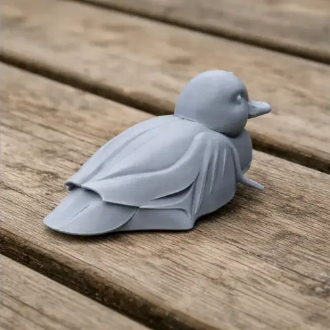 A gray 3D-printed model of a Baikal teal duck resting on a wooden surface.
