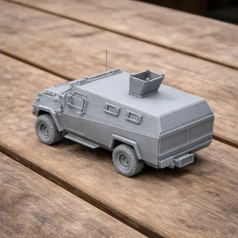 Gray 3D-printed model of an armored personnel carrier with detailed wheels and turret on a wooden surface.