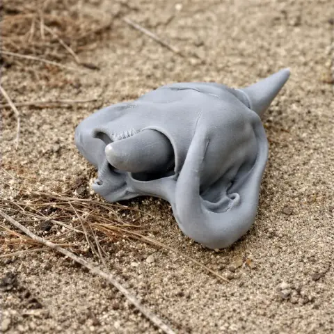 3D printed Syncerus antiquus skull replica, gray, resting on sandy ground with twigs.