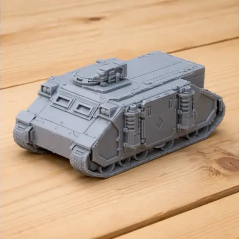 Gray 3D-printed model of an armored personnel carrier with treads and mounted turret on a wooden surface.