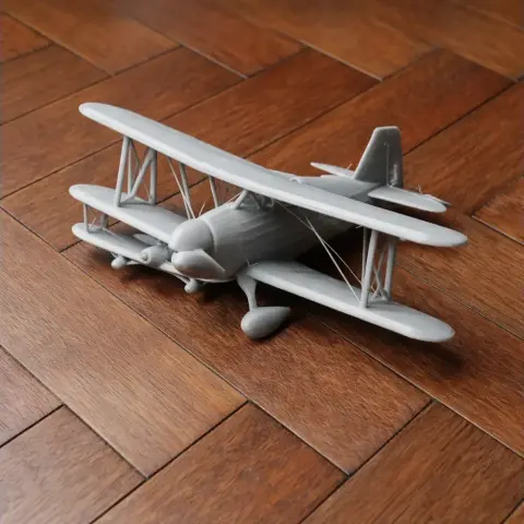 A 3D-printed model of a biplane with detailed wings and propeller, placed on a wooden floor.