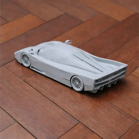 A detailed 3D printed model of a sleek, aerodynamic race car on a wooden floor.