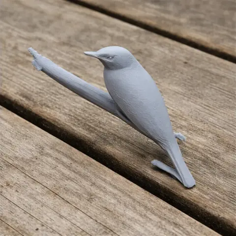 Gray 3D-printed bird model perched on a branch, placed on a wooden surface.