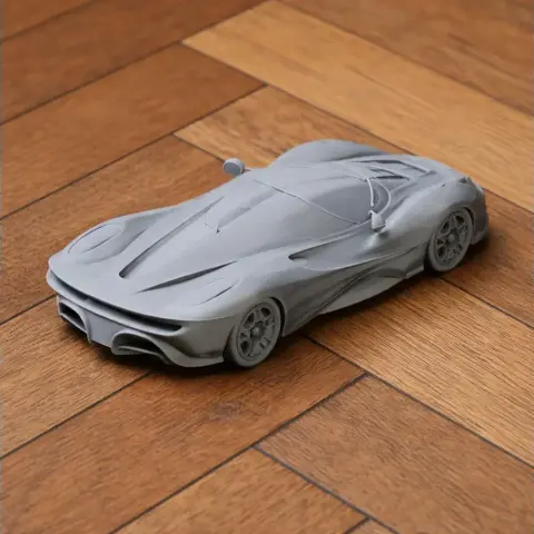 3D printed gray scale model of a sleek, futuristic car on a wooden floor.