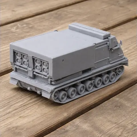 Gray 3D-printed model of a multiple rocket launcher tank with tracks, on a wooden surface.