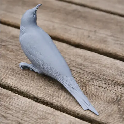 Gray 3D-printed model of a bird with detailed feathers, posed on a wooden surface.