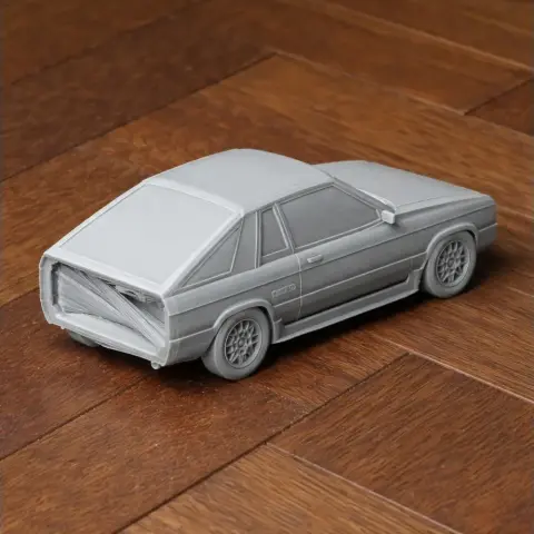 Gray 3D-printed model of a Dodge Omni 024 car on a wooden surface.