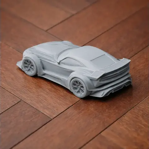 3D-printed gray model of a sleek sports car on a wooden surface.