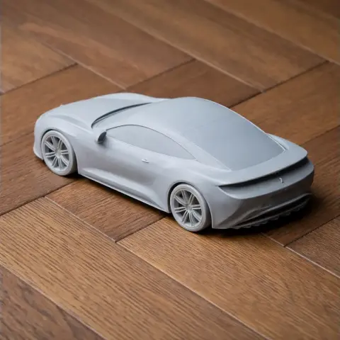 A sleek, unpainted 3D-printed model of a modern sports car on a wooden surface.