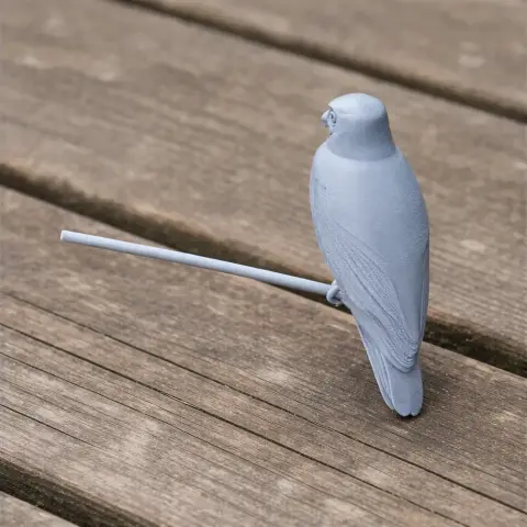 Gray 3D-printed owl model perched on a stick, placed on a wooden surface.