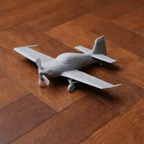 A grey 3D-printed model of a small airplane with a propeller on a wooden surface.