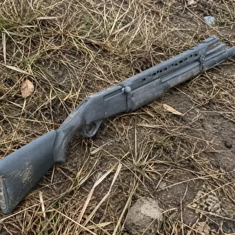 A 3D printed Benelli M2 cosplay prop laying on dry grass and dirt.