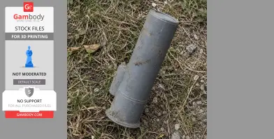 A gray, cylindrical cosplay prop resembling a breaching round, lying on grass and gravel.