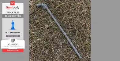 A 3D-printed gray cane gun prop lying on grass and dirt.