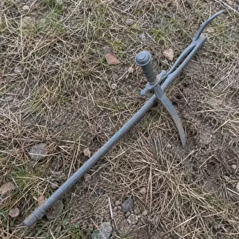 A detailed, gray 3D-printed sword prop with intricate design, lying on dry grass.