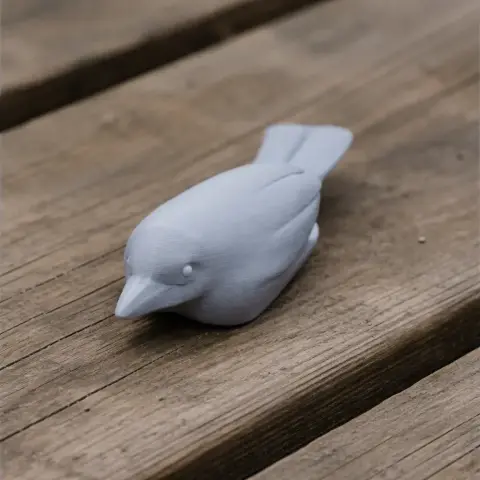 A small 3D-printed bird model, grey in color, resting on a wooden surface.